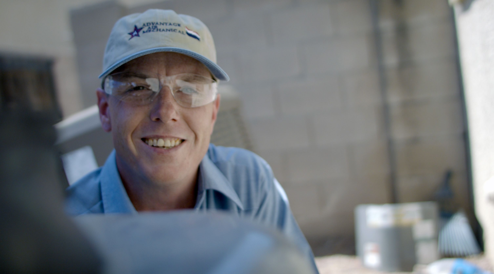 A uniformed Advantage Air tech wearing clear safety glasses smiling at the camera.