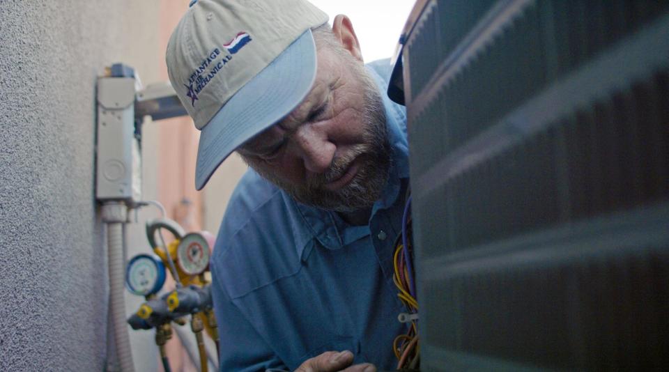Advantage Air Mechanical technician wearing a branded baseball cap, inspecting the back of a heat pump