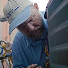 Advantage Air Mechanical technician wearing a branded baseball cap, inspecting the back of a heat pump