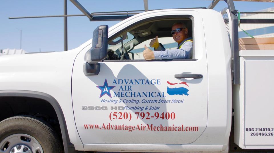 An Advantage Air tech is in the driver's eat of a branded service truck with his window down smiling and giving a double thumbs up to the camera.