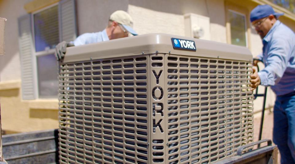 Two uniformed Advantage Air Mechanical technicians moving a York cooling system from the back of a truck and next to a home.