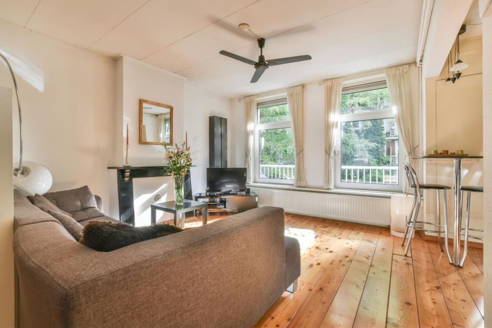 Living room with gray couch, hardwood floors, white curtains, and a black fireplace