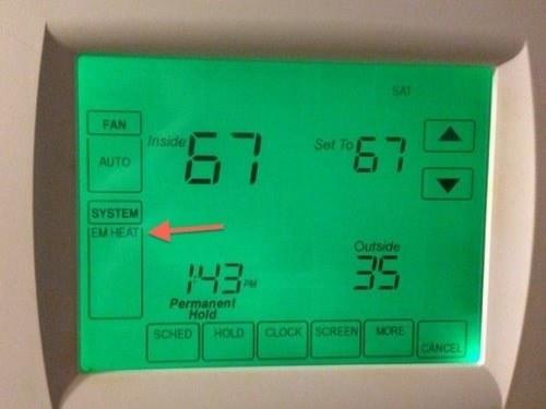 Closeup of a thermostat screen lit up green with a red arrow pointing to "EM HEAT".