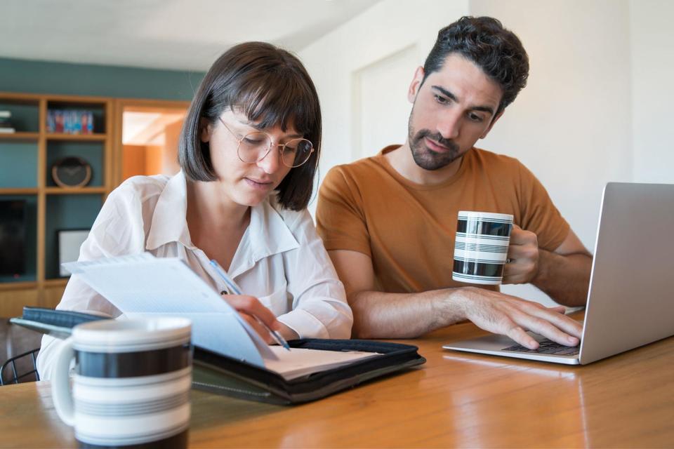 A couple sitting at a table, reviewing notes together with an opened silver laptop nearby.