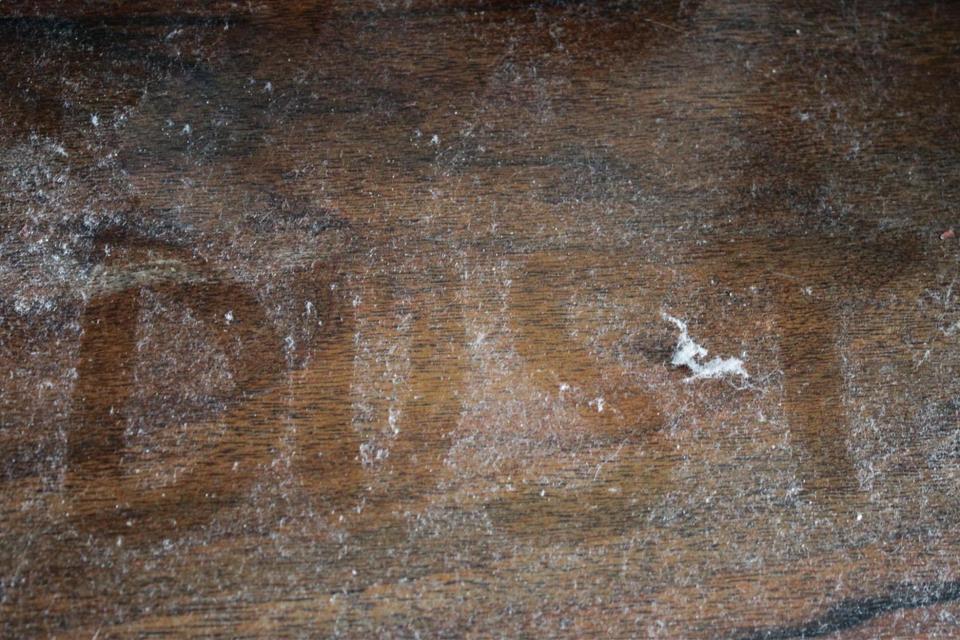 The word "Dust" written on a dusty wooden table.