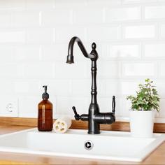 A white kitchen sink with a black faucet, installed in a wooden countertop, with a white tiled backsplash behind it.