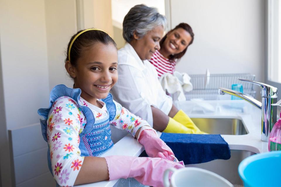 A grandmother, mother, and daughter washing dishes in a double basin sink.