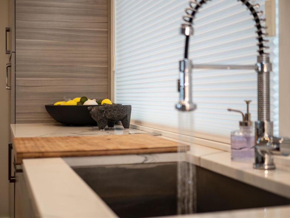 A stainless steel kitchen faucet with water spraying out of it into a one basin gray sink installed in a white marble kitchen countertop.