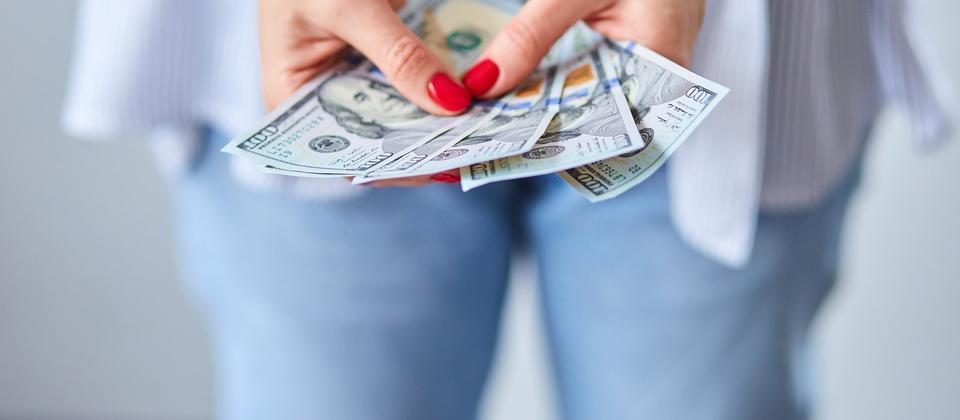 Closeup of a woman's hands with bright red painted nails and holding four $100 bills in her hands