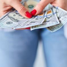 Closeup of a woman's hands with bright red painted nails and holding four $100 bills in her hands