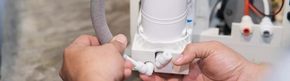 A closeup of a person working on a connection to the bottom of a water softener system.