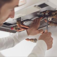 Close up of a tech wearing a white long sleeve shirt, using a wrench to tighten a pipe fitting at the bottom of a water heater.