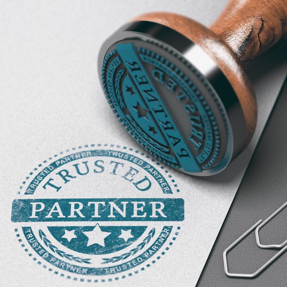 A rubber stamp that says Trusted Partner on it dipped in teal ink and stamped on heathered gray paper with a paperclip sitting next to it.