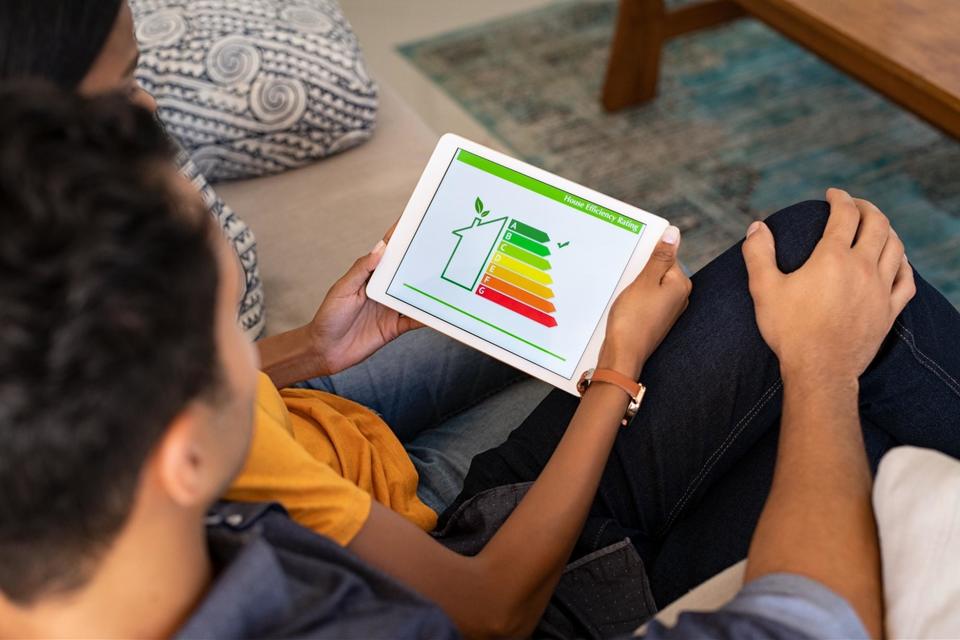 A dad and child sitting on the couch together looking at an energy efficiency app that the kid is holding.