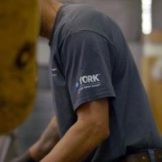 A man working in a shop wearing a blue gray t-shirt that has the York logo on the left sleeve