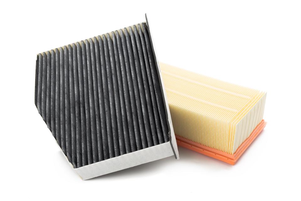 A small black air filter tilted on top of a cream air filter.