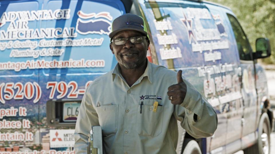 A uniformed Advantage Air tech standing behind his branded service van, holding a clipboard and giving a thumbs up to the camera