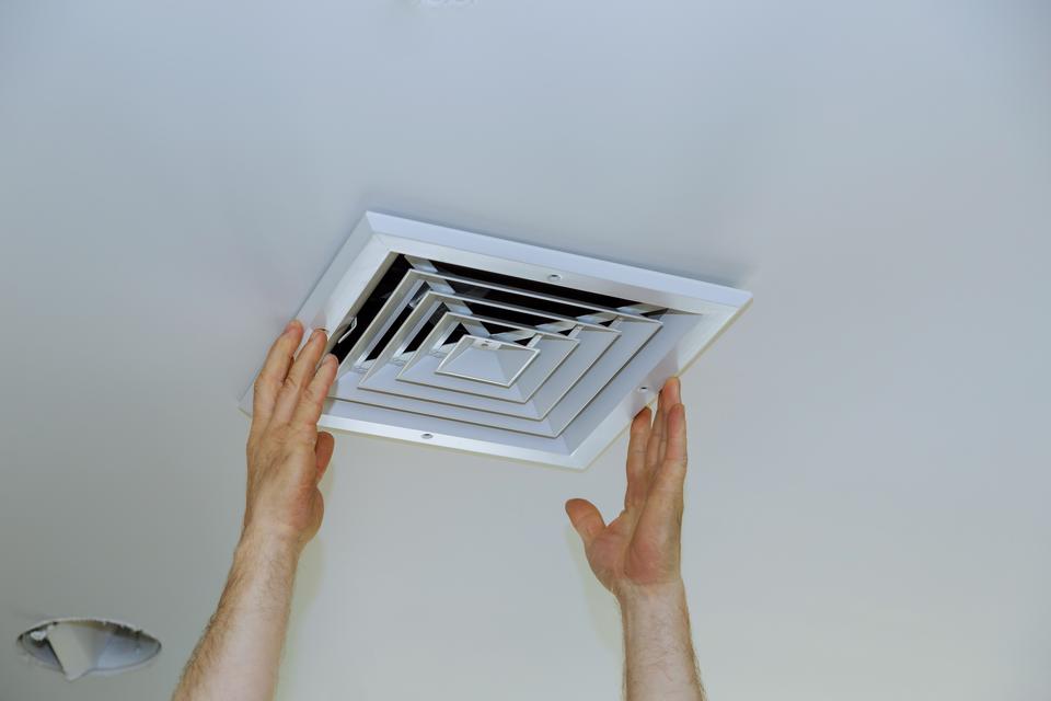 Close up of a man's hands installing a vent cover on ceiling